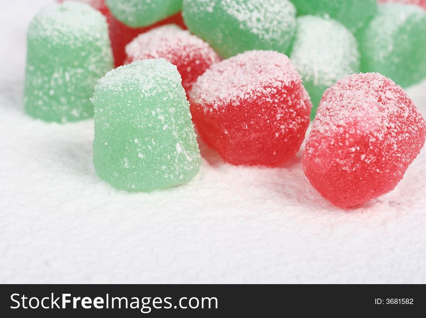 A close up of red and green spiced gumdrops covered in snow. A close up of red and green spiced gumdrops covered in snow.