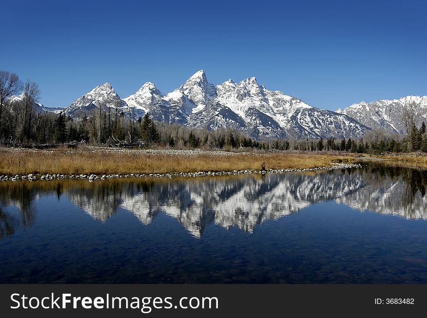 Detail of Grand Tetons Mountains with blue sky with reflection in river. Detail of Grand Tetons Mountains with blue sky with reflection in river