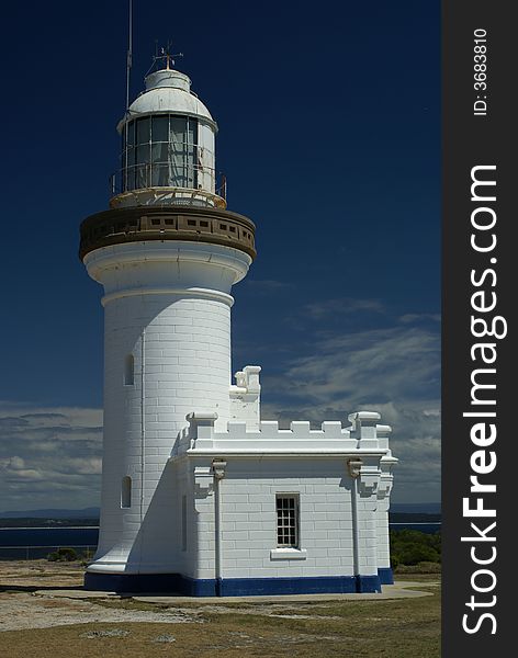 White lighthouse with blue base contrasting with blue sky with whit clouds below