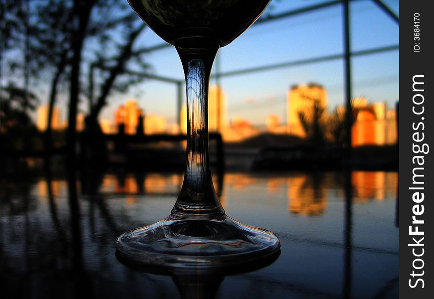 A glass of wine on the table reflecting the buildings at the sunset. A glass of wine on the table reflecting the buildings at the sunset.