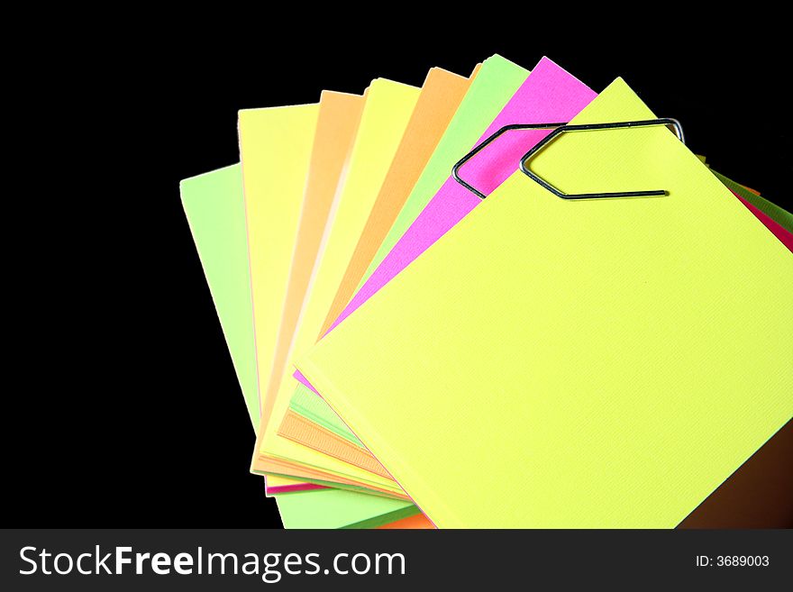 Colored paper notes over black background and joined by clips