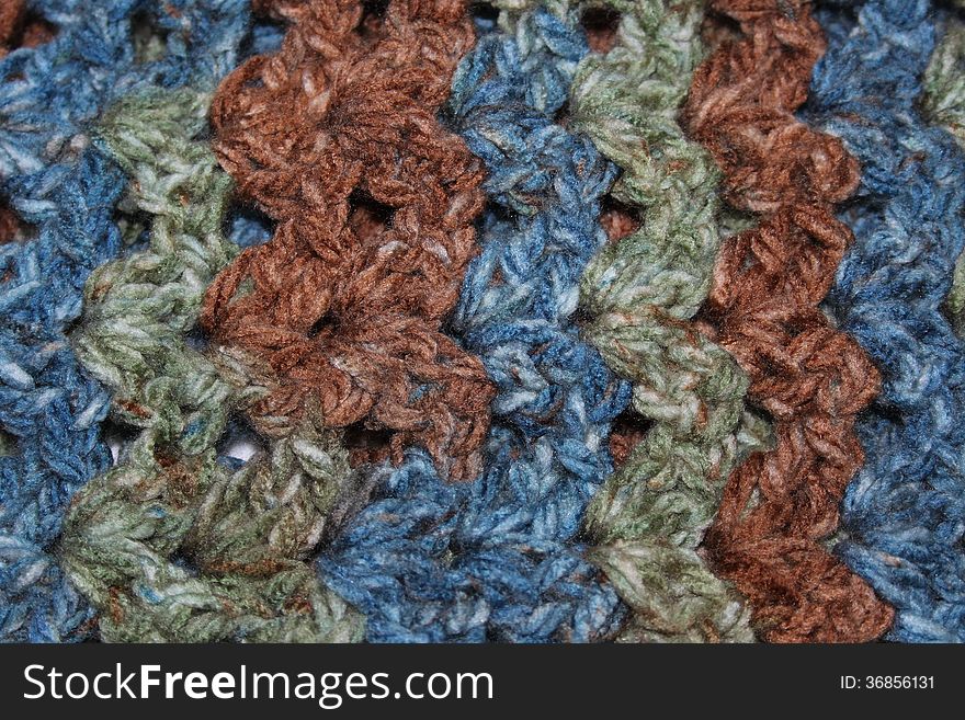 Closeup of crochet fabric with vertical blue, green, and brown stripes. Closeup of crochet fabric with vertical blue, green, and brown stripes.