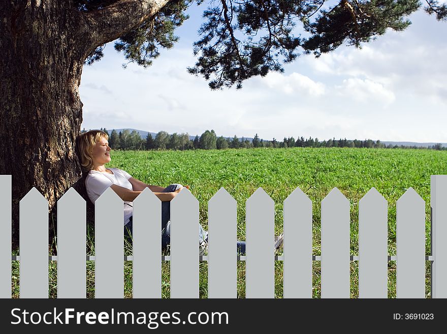 Young beauty woman sit under alone tree in field under blue sky and clouds