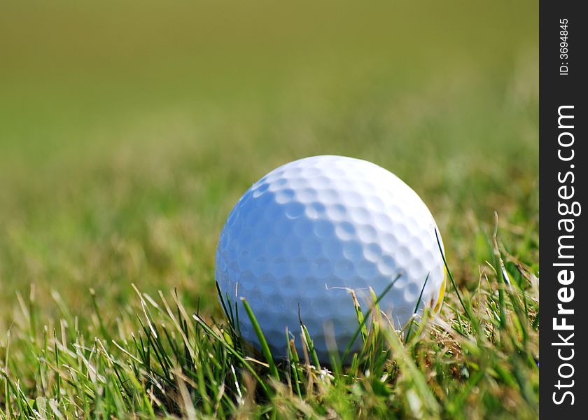 Golf ball on grass taken with a long lens giving shallow depth of field. Space on left hand side for text. Golf ball on grass taken with a long lens giving shallow depth of field. Space on left hand side for text.
