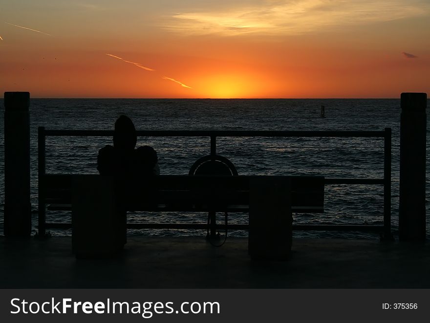 Man sitting on bench at pier at sun set. Man sitting on bench at pier at sun set