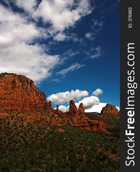 Some cliffs in the foreground against a blue sky with some clouds. The desert is quite green because of recent rain that caused growth in the summer. This location is near Sedona a very popular vacation spot. Some cliffs in the foreground against a blue sky with some clouds. The desert is quite green because of recent rain that caused growth in the summer. This location is near Sedona a very popular vacation spot.