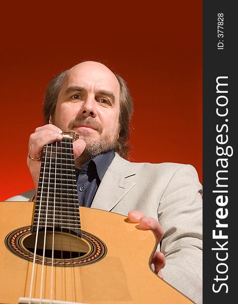 Middle aged man-musician with his guitar on a red background. Focused on the hand near his face, the face is slightly out of focus.