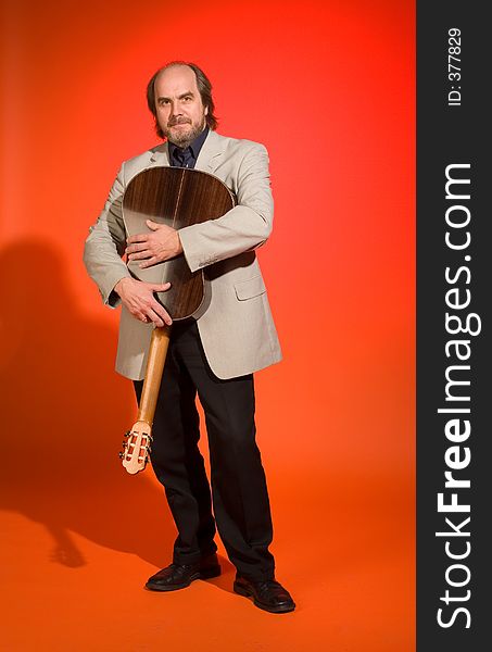 Middle aged man-musician holding dear his guitar on a red background.