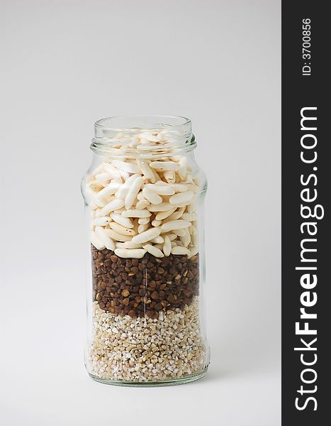 Tall glass jar, isolated, filled with three kinds of grain. Tall glass jar, isolated, filled with three kinds of grain