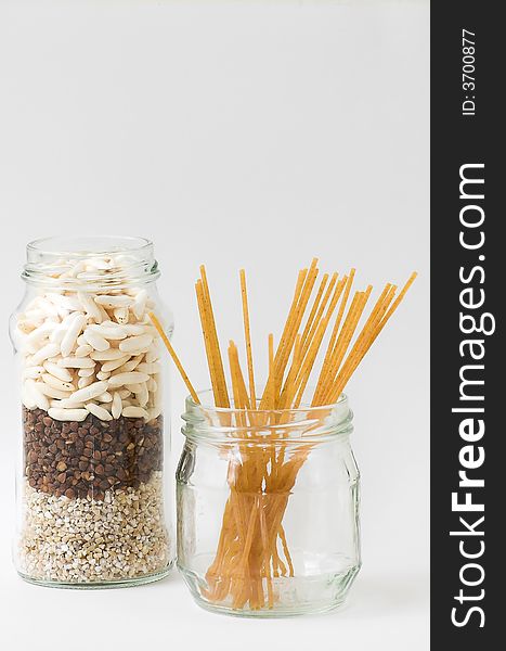 Two glass jars, isolated, filled with three kinds of grain and spaghetti. Two glass jars, isolated, filled with three kinds of grain and spaghetti