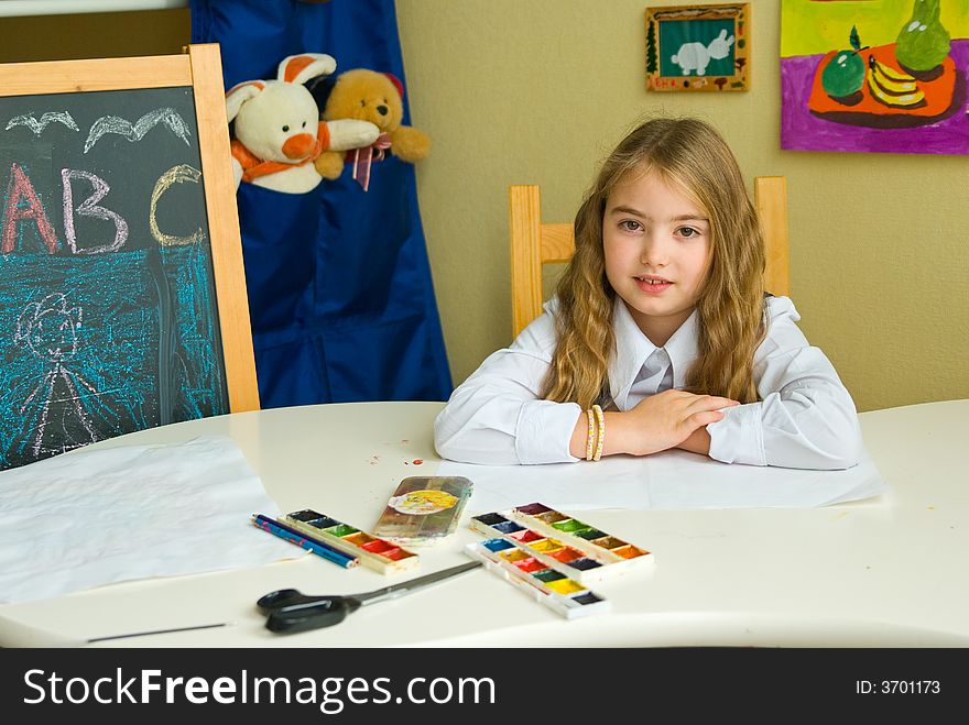 Schoolgirl sits at the table with paint