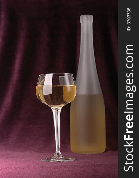 Glass and bottle of white wine on a background of an elegant velveteen material of claret color