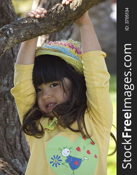 Cute little girl in yellow top and rainbow hat hanging from a tree. Cute little girl in yellow top and rainbow hat hanging from a tree