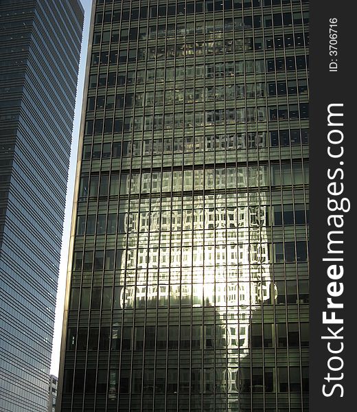 The picture display a close up of two skyscrapers. On the glassy surface of the skyscrapers on the right it is visible the reflection of another skyscraper. The picture display a close up of two skyscrapers. On the glassy surface of the skyscrapers on the right it is visible the reflection of another skyscraper