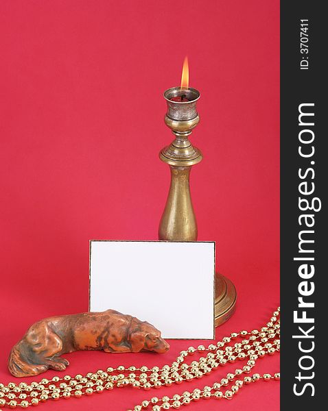 Christmas candle with flame. A white card in front. Red background.