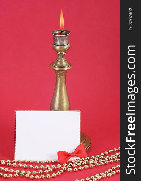 Christmas candle with flame. A white card in front. Red background.