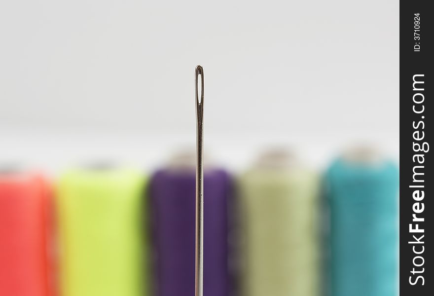 Colorful bobbins blurred in the background, close up of a needle. Colorful bobbins blurred in the background, close up of a needle