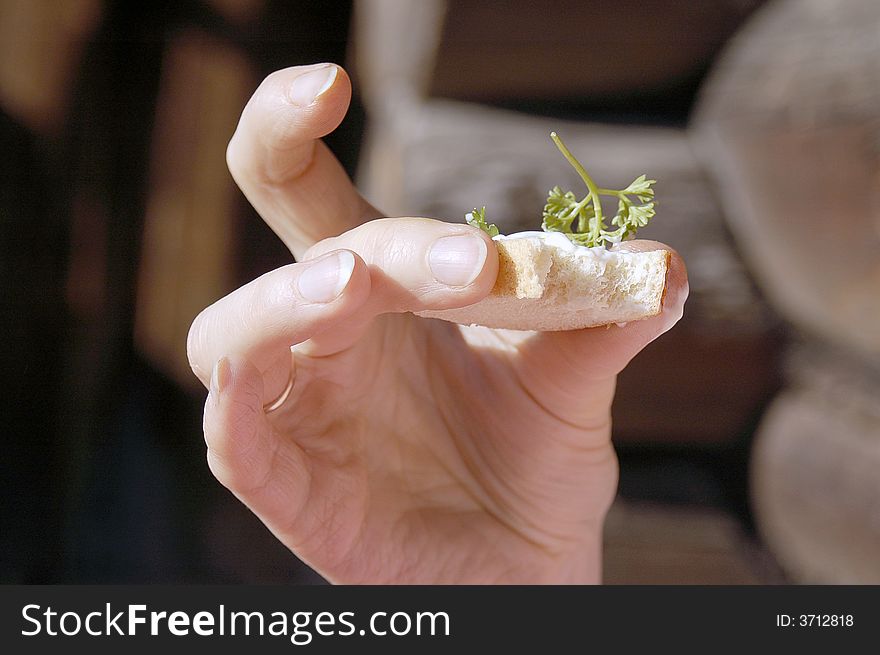 Small part of a sandwich with a parsley in a female hand on a background of a wooden wall. Small part of a sandwich with a parsley in a female hand on a background of a wooden wall