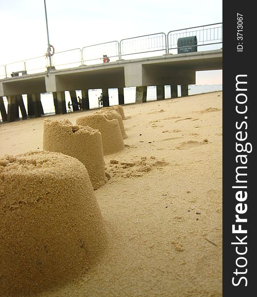 A line of sand castles on the beach standing high and strong, just like the jetty behind it. A line of sand castles on the beach standing high and strong, just like the jetty behind it.