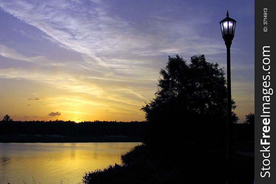 Street lamp and sunset at lake shore illuminate simultaneously