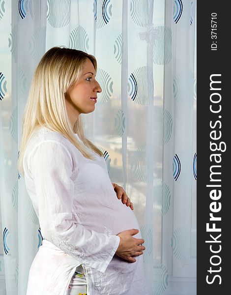Caucasian pregnant woman near window at home.