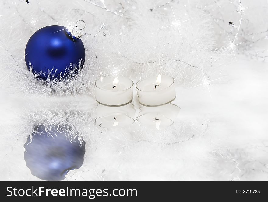 Candles and frosted blue Christmas ornament surrounded by sparkling, snowy tinsel and ice. Candles and frosted blue Christmas ornament surrounded by sparkling, snowy tinsel and ice