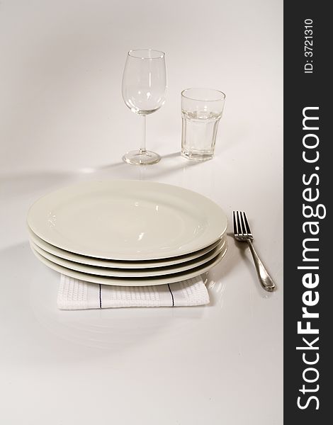 Table setting of four stacked classic plates , napkin , silver fork, wines glass and glass cup. Table setting of four stacked classic plates , napkin , silver fork, wines glass and glass cup.