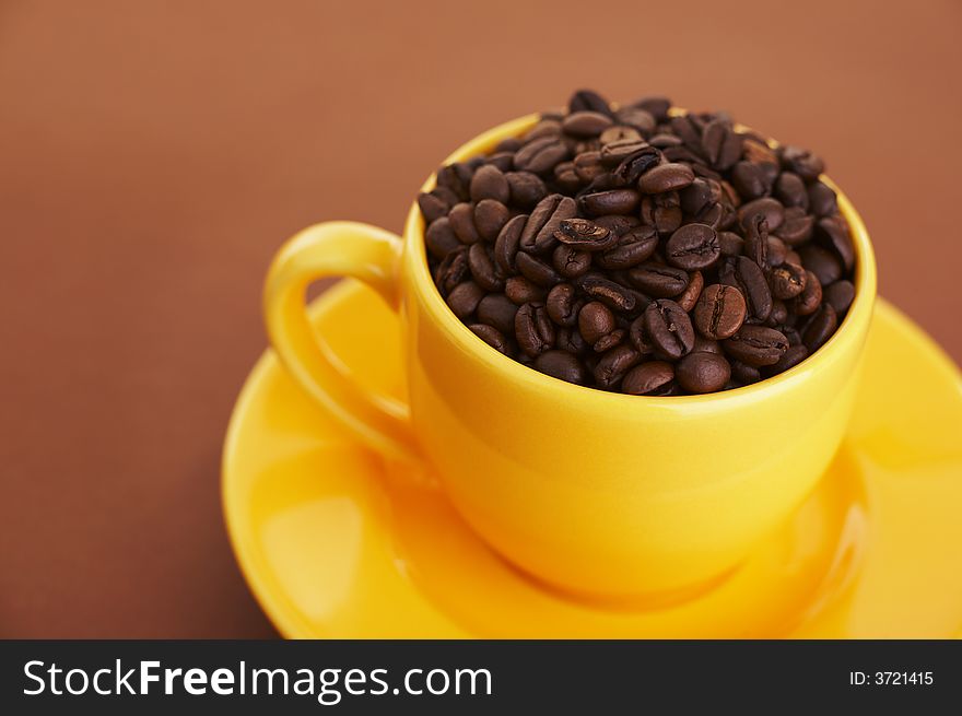 Yellow coffee cup filled with coffee beans over a brown background (shallow dof)