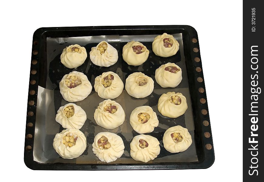 The isolated image of the small meat pies on the baking sheet covered with oiled paper