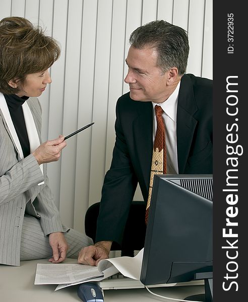 A man and a woman in an office setting appearing to be co-workers engaged in discussion. A man and a woman in an office setting appearing to be co-workers engaged in discussion.