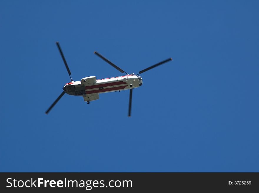 A twin rotor helicopter flying overhead against a blue sky. A twin rotor helicopter flying overhead against a blue sky