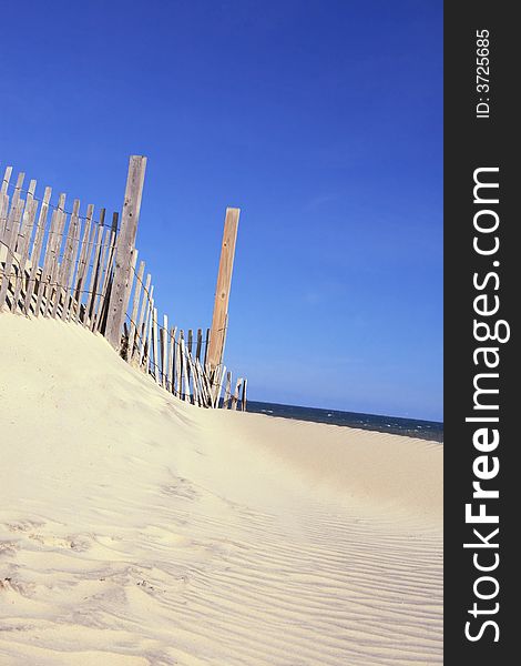 View of a sandy beach leading towards the ocean, small fence. View typical of many coastal, beach-front communities. View of a sandy beach leading towards the ocean, small fence. View typical of many coastal, beach-front communities