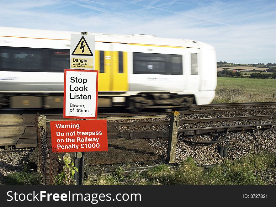 Fast train passing through railway pedestrian crossing, at which multiple warning signs are displayed.