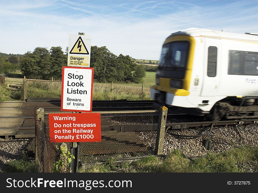 Fast train approaching railway pedestrian crossing, at which multiple warning signs are displayed.