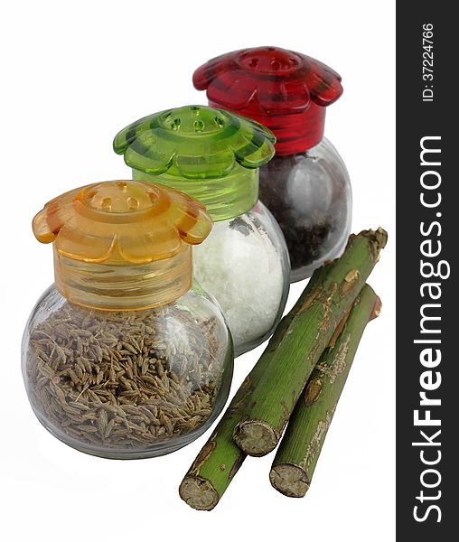 Three glass jars with multi-colored covers with spices and green stalks on a white background. Three glass jars with multi-colored covers with spices and green stalks on a white background