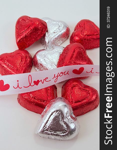 I Love You ribbon crossing red and silver chocolate candy hearts on white background. I Love You ribbon crossing red and silver chocolate candy hearts on white background
