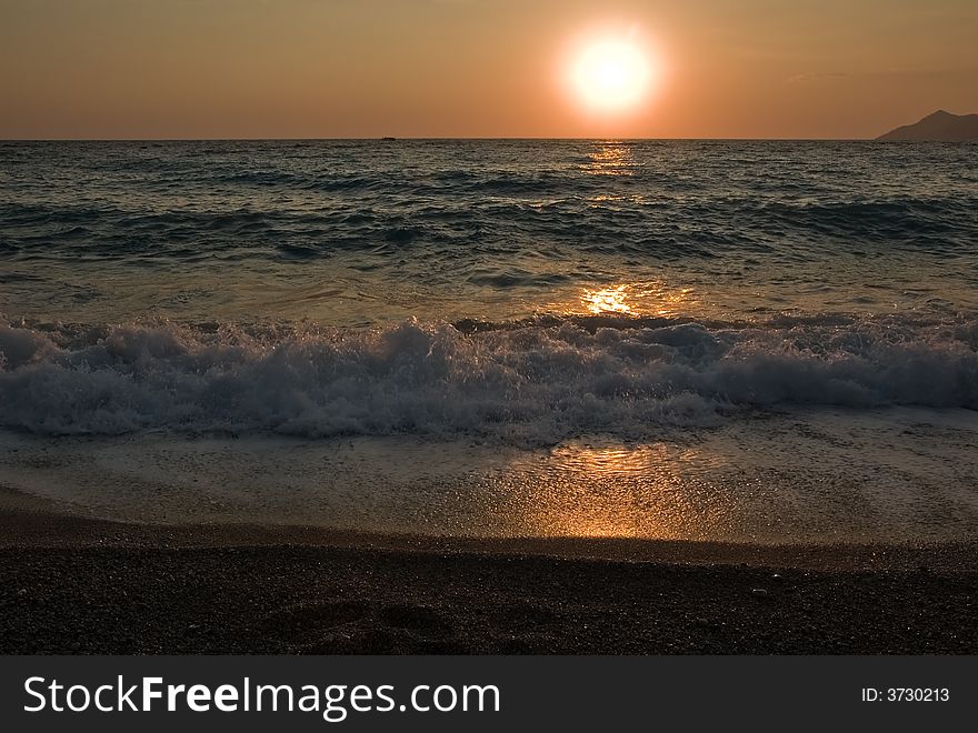 Photo of sun sets beyond the sea and higlights its waves. Photo of sun sets beyond the sea and higlights its waves