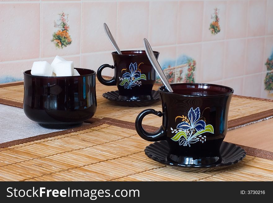 Photo of two black tea cups accompanied by sugar-bowl with bits of sugar. Photo of two black tea cups accompanied by sugar-bowl with bits of sugar