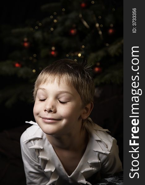 Smiling boy with closed eyes near a new year tree with decorations. Smiling boy with closed eyes near a new year tree with decorations