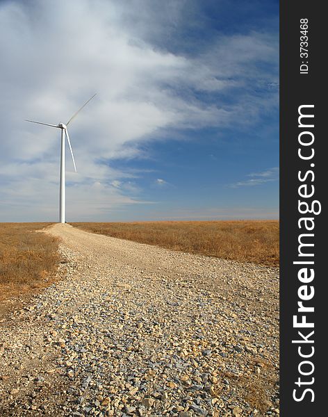 A gravel road leads up to a large white wind turbine. A gravel road leads up to a large white wind turbine.