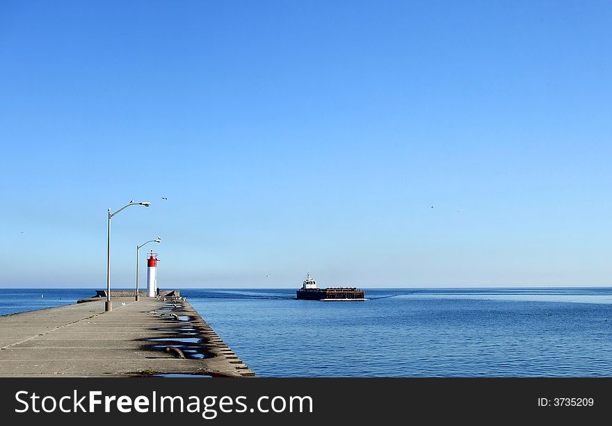 A barge approaches near the pier and a small lighthouse.