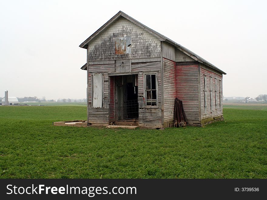 An old one room school house in a field on a cloudy day.