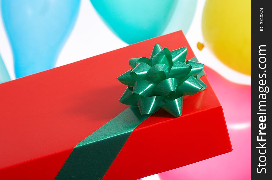 A red giftbox with green ribbon over the balloon background. A red giftbox with green ribbon over the balloon background