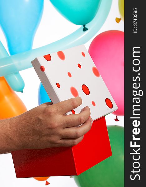 A hand holds a red gift box over the balloons. A hand holds a red gift box over the balloons