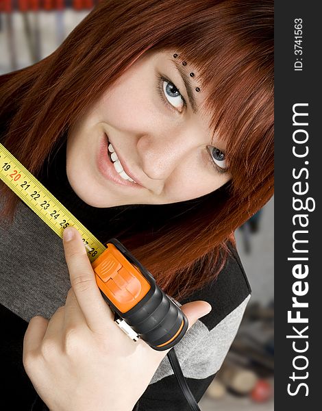 Beautiful redhead girl using measuring tape in workshop and pointing at 25cm.Studio shot.