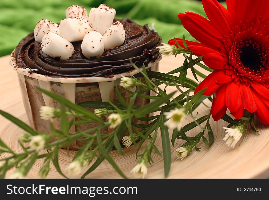 A chocolate cup cake with marshmallow toppings decorated with a red daisy. A chocolate cup cake with marshmallow toppings decorated with a red daisy