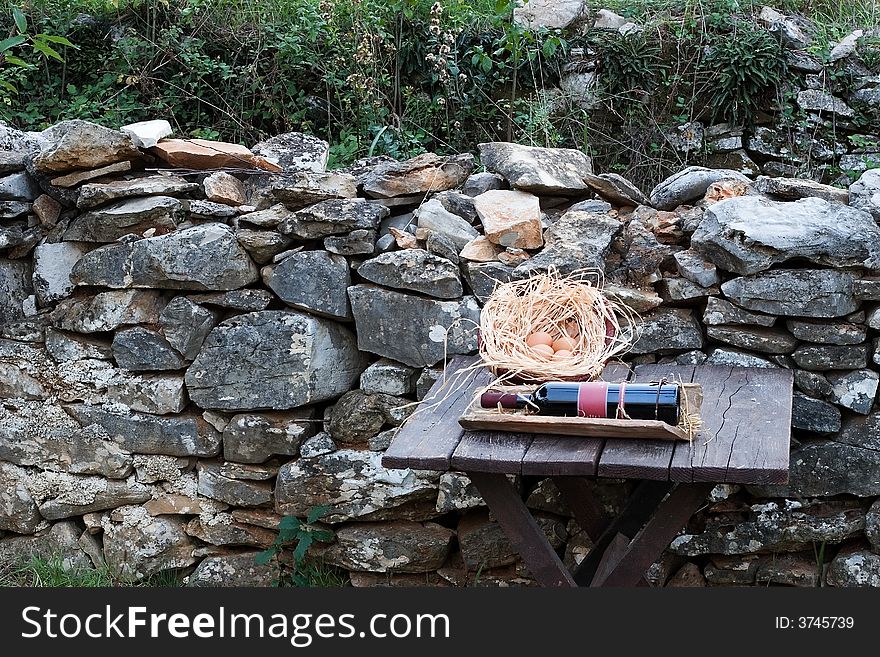 Eggs and wine on table in garden near stone wall. Eggs and wine on table in garden near stone wall