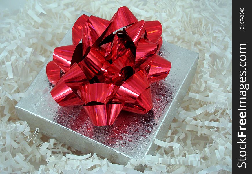A present in a silver box with a red ribbon on top.