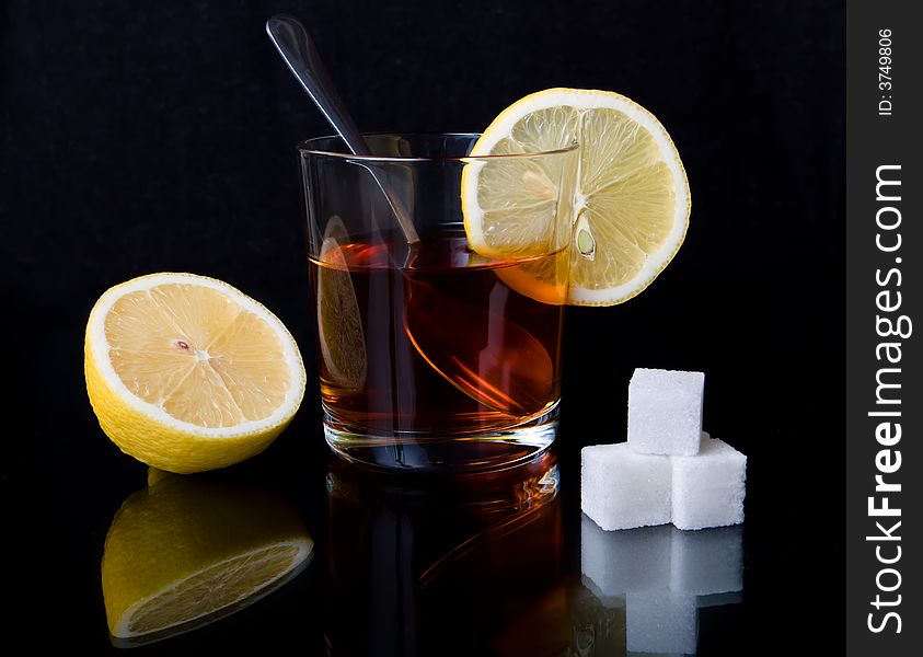 Glass with tea, the spoon, sugar and a lemon on a black reflecting surface. Glass with tea, the spoon, sugar and a lemon on a black reflecting surface