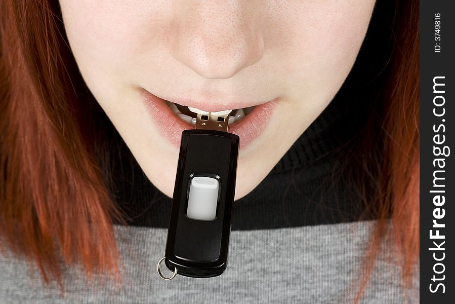 Close-up of a redhead girl biting a flash drive / memory stick, usb.

Studio shot.